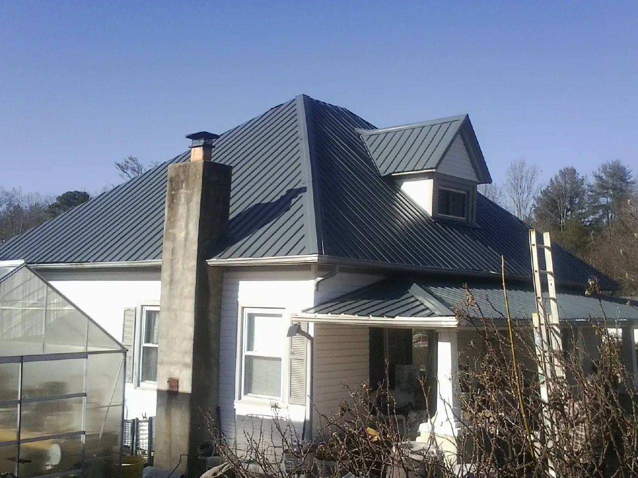 Dark blue standing seam metal roof on a white farmhouse with dormer — Slate & Tile Roof Repair by Roofing Brothers in Brea
