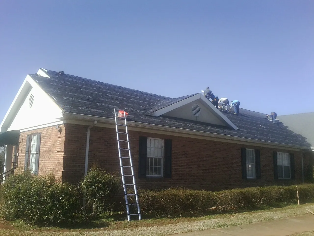 Crew tearing shingles off a brick ranch roof with a ladder set — Metal Roof Repair work by our crew in Brea