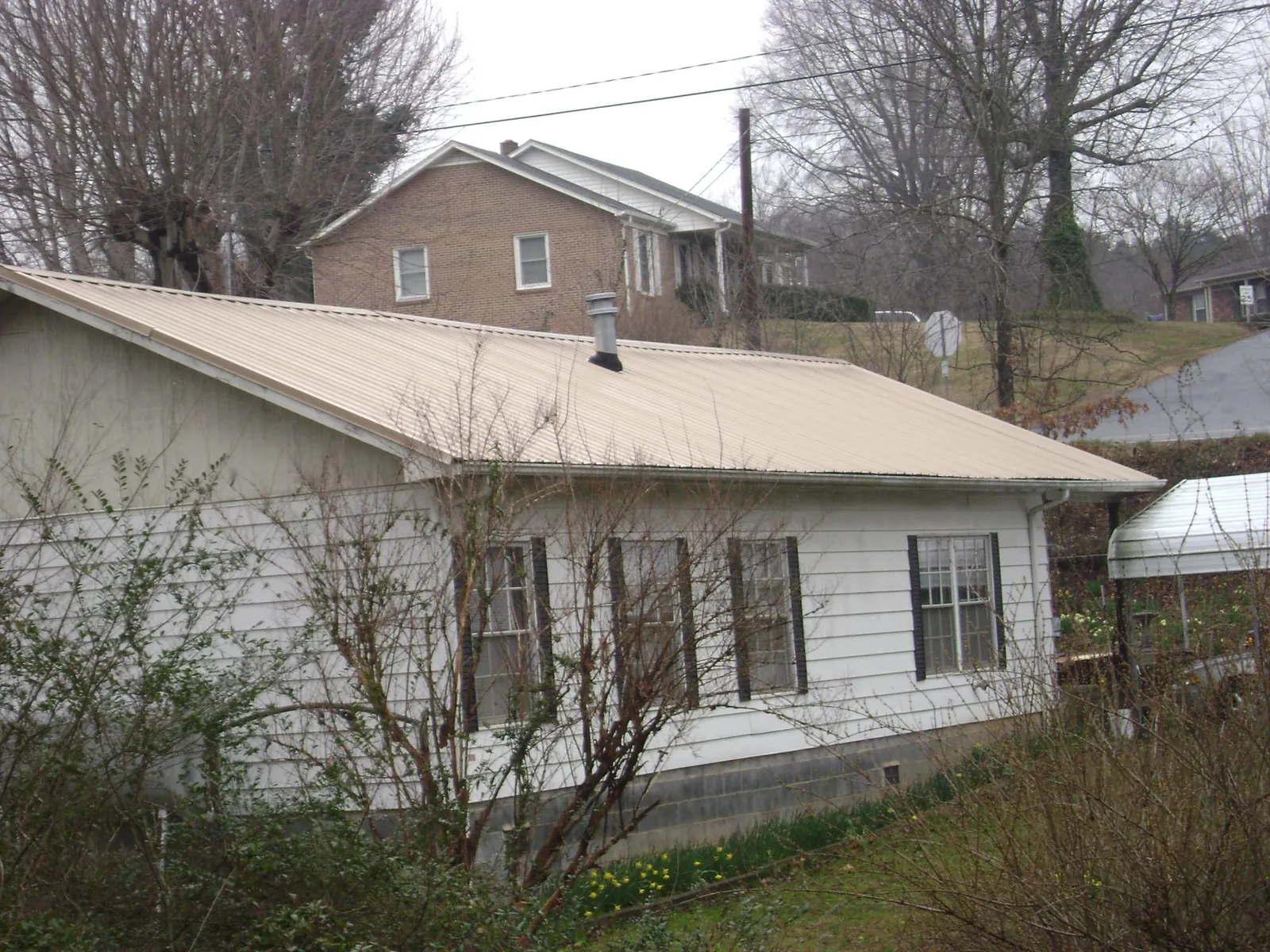 Tan metal roof on a white sided house set into a hillside — Commercial Roofing by Roofing Brothers in Brea